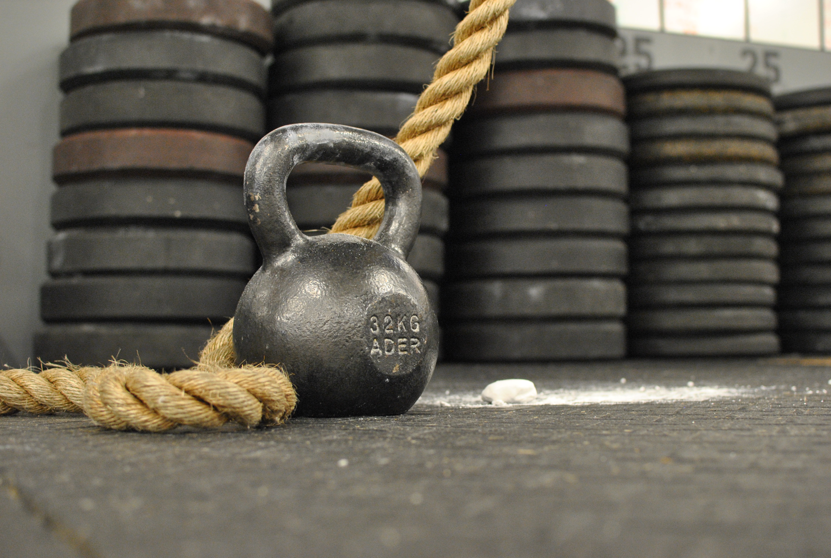 A kettlebell sits in front of a climbing rope with chalk in the background